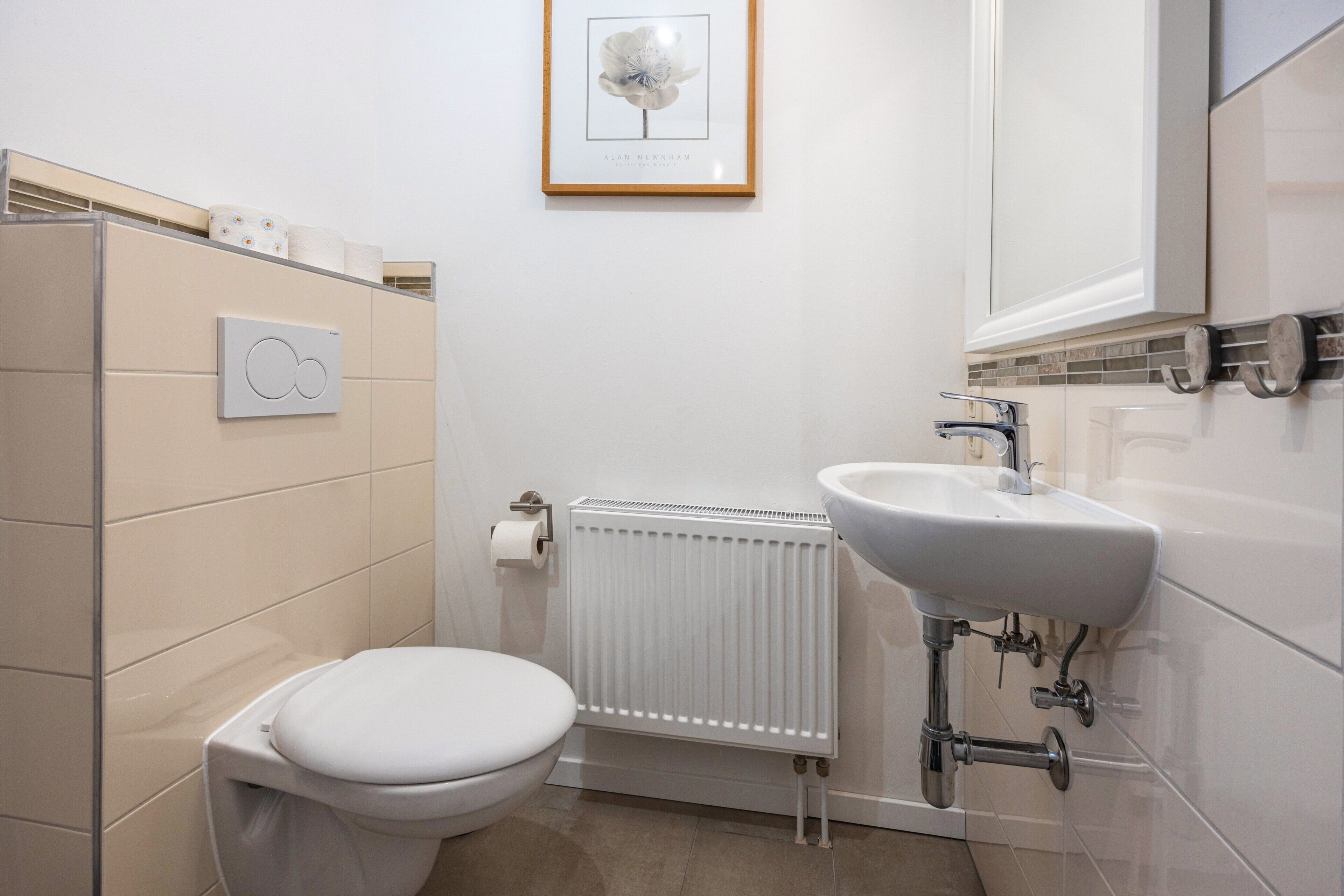 Un baño moderno con inodoro, radiador, lavamanos y un cuadro en la pared.