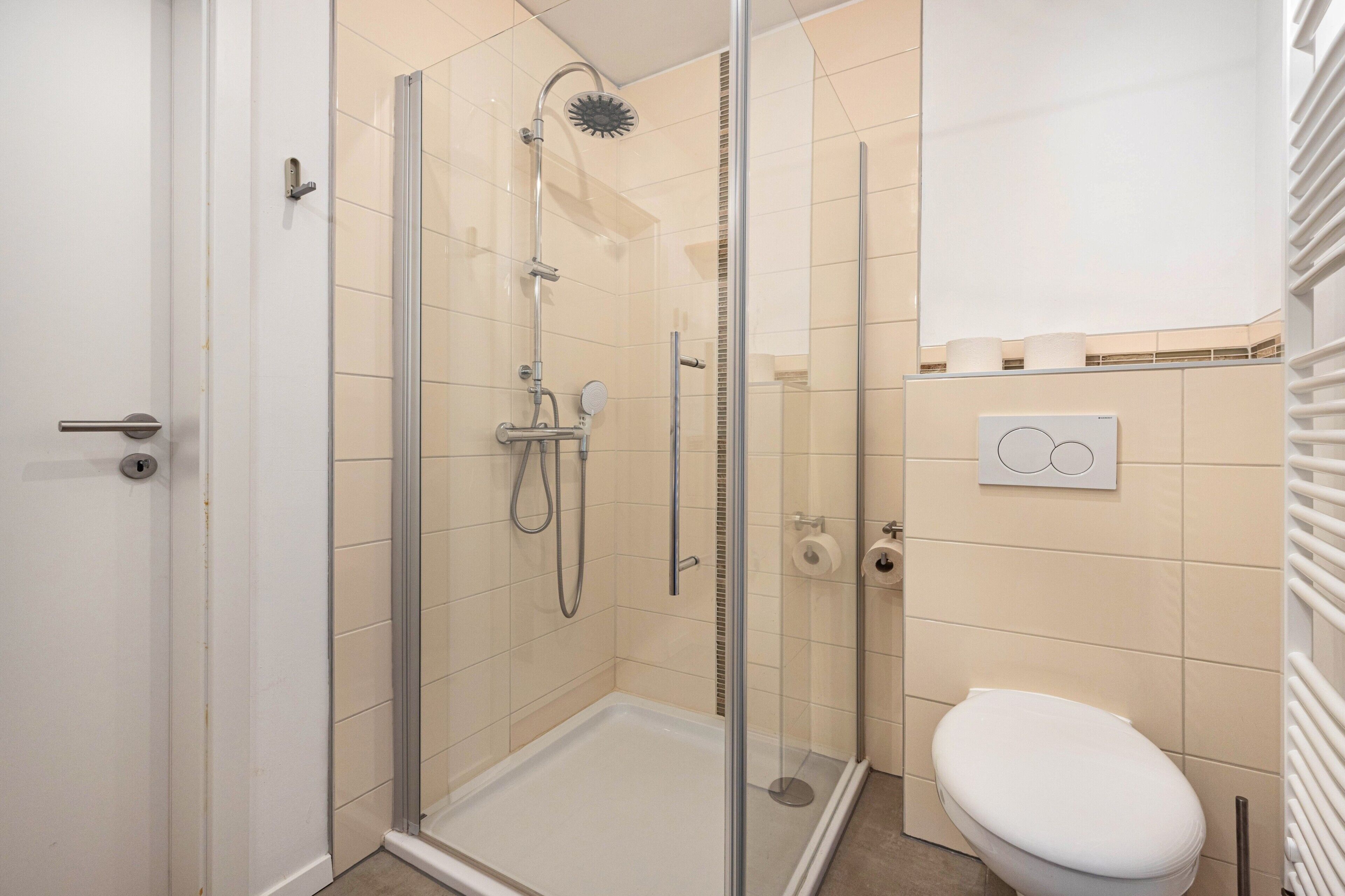 Een badkamer met een douche met glazen wand, een toilet en een handdoekhouder.