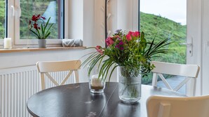 Une table à manger avec des chaises, un vase rempli de fleurs, une bougie et une fenêtre donnant sur un paysage verdoyant.