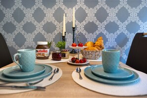 A dining table set with plates, cups, and a basket of croissants, with a jar of Nutella and a candle holder in the background. - Apartment 'Süsse 2 Zimmerwohnung' with Private Terrace and Wi-Fi (Heiligenstedten)