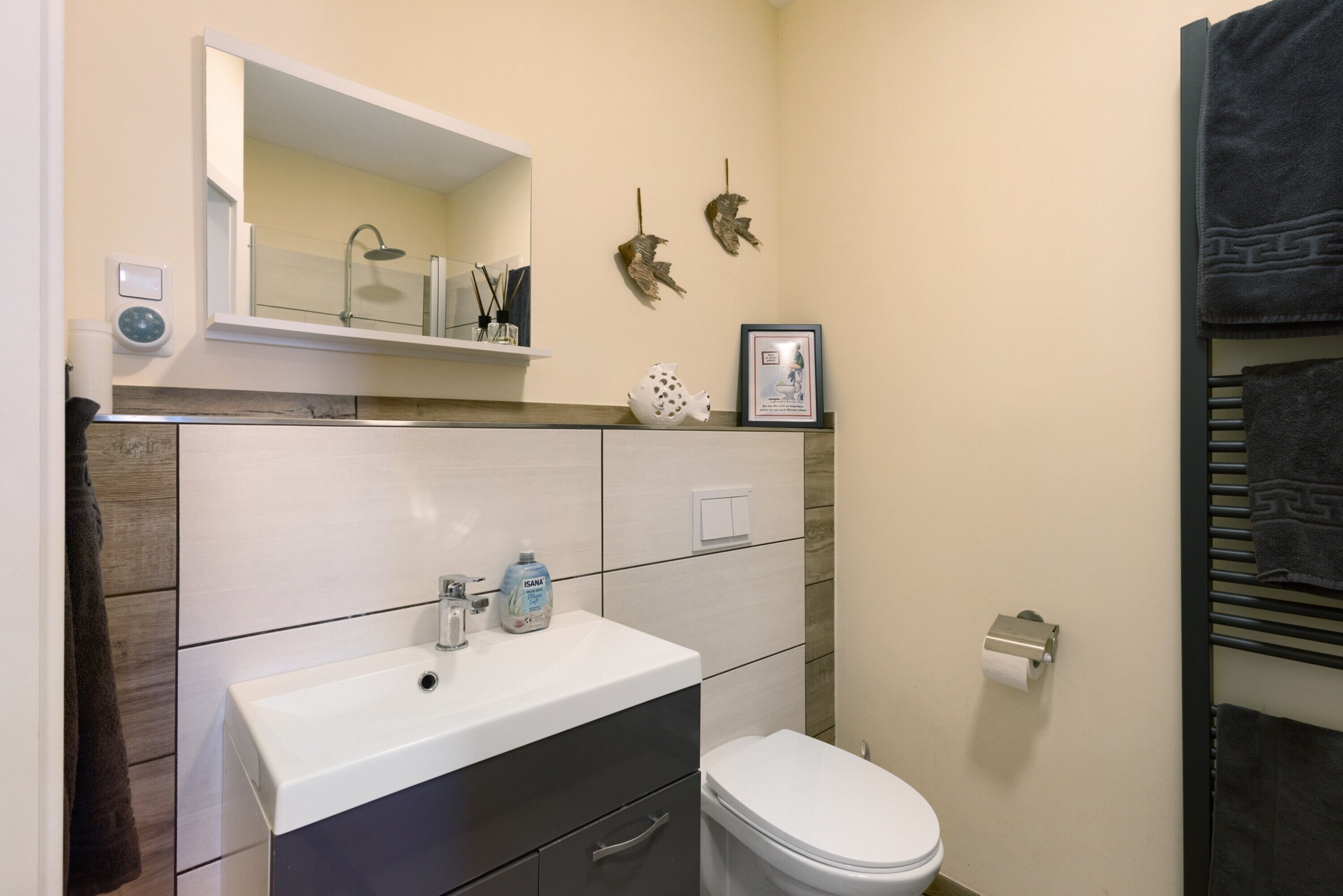 Un baño con lavamanos blanco, inodoro, espejo y toallero.