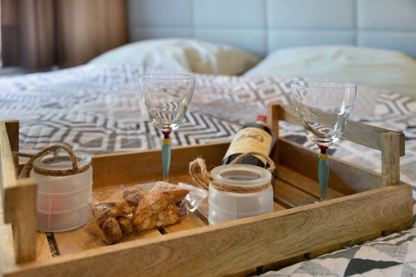 Una bandeja de madera con dos vasos, una botella y una bolsa de aperitivos sobre una cama con ropa de cama estampada.