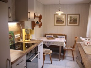 Een keuken met een oven, een koffiezetapparaat en een eettafel met stoelen.