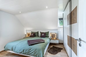 Une chambre moderne avec un plafond en pente, un lit avec une literie verte, un plancher en bois et une vue sur l’extérieur.