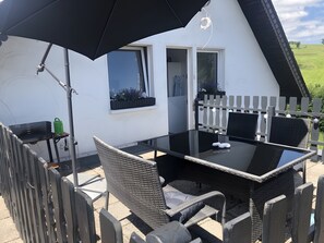 Une terrasse avec une table et des chaises, un barbecue et un parasol noir.