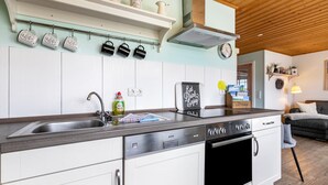 A modern kitchen with white cabinets, stainless steel appliances, and a wooden ceiling. - Apartment 'Doppelhaushälfte Ida' with Private Terrace, Shared Garden and Wi-Fi (Meldorf)