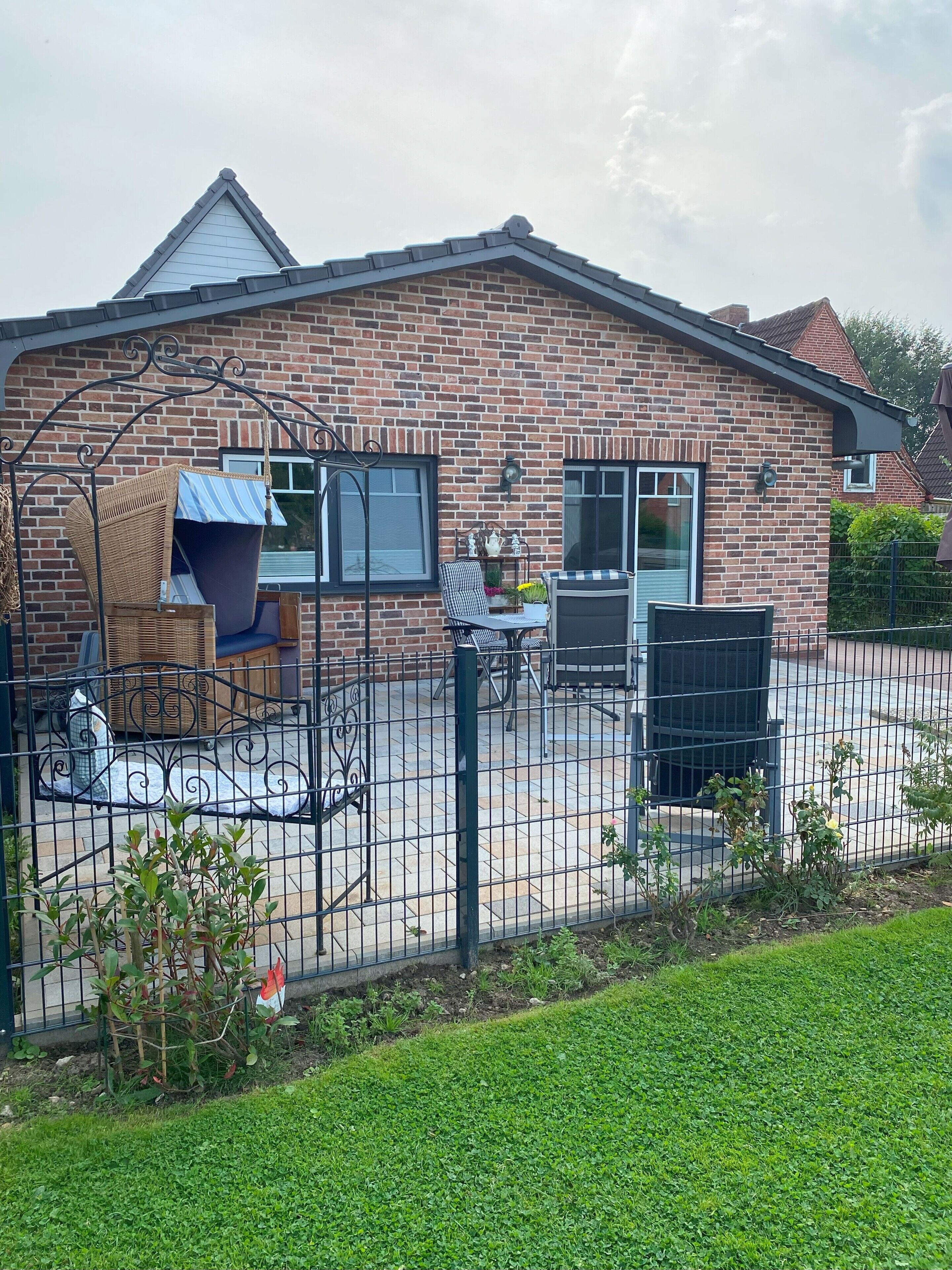 Een bakstenen huis met een omheinde achtertuin, een schommel en tuinmeubilair.