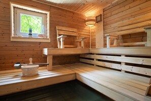 Un sauna en bois, avec des bancs, un seau et une fenêtre donnant sur la verdure.