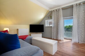 Een woonkamer met een bank, een poef, een televisie en een raam met gordijnen.