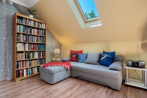 Een gezellige woonkamer met een hoekbank, een boekenkast, een bijzettafeltje met een lamp en een dakraam.