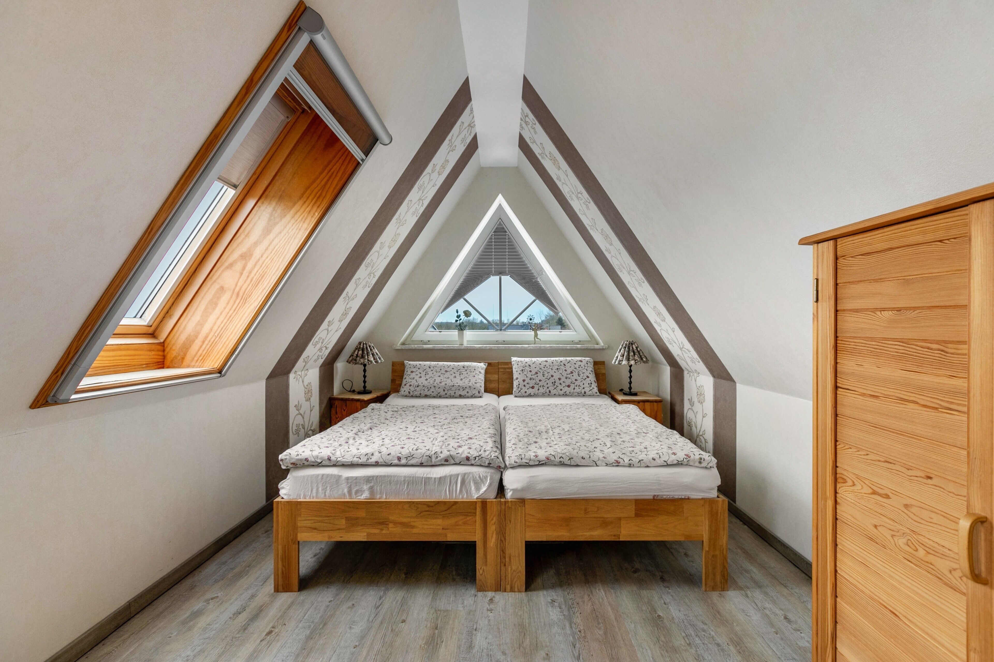 Ein Schlafzimmer mit Schrägdecke, einem Oberlicht, einem Bett mit Holzrahmen, Nachttischen und einem Kleiderschrank.