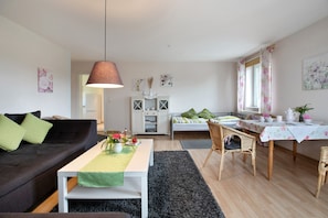 A living room with a sofa, coffee table, dining table, and a kitchen area in the background.