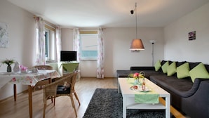 Un salon avec un canapé, une table à manger, un téléviseur et une fenêtre avec des rideaux.