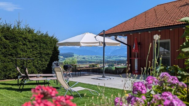 Une terrasse avec des meubles d’extérieur, un parasol blanc et une vue sur les montagnes.