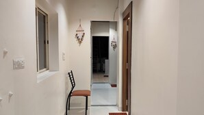 A hallway with a chair, a wooden door, and a window. - Magick Oven (Ujjain)
