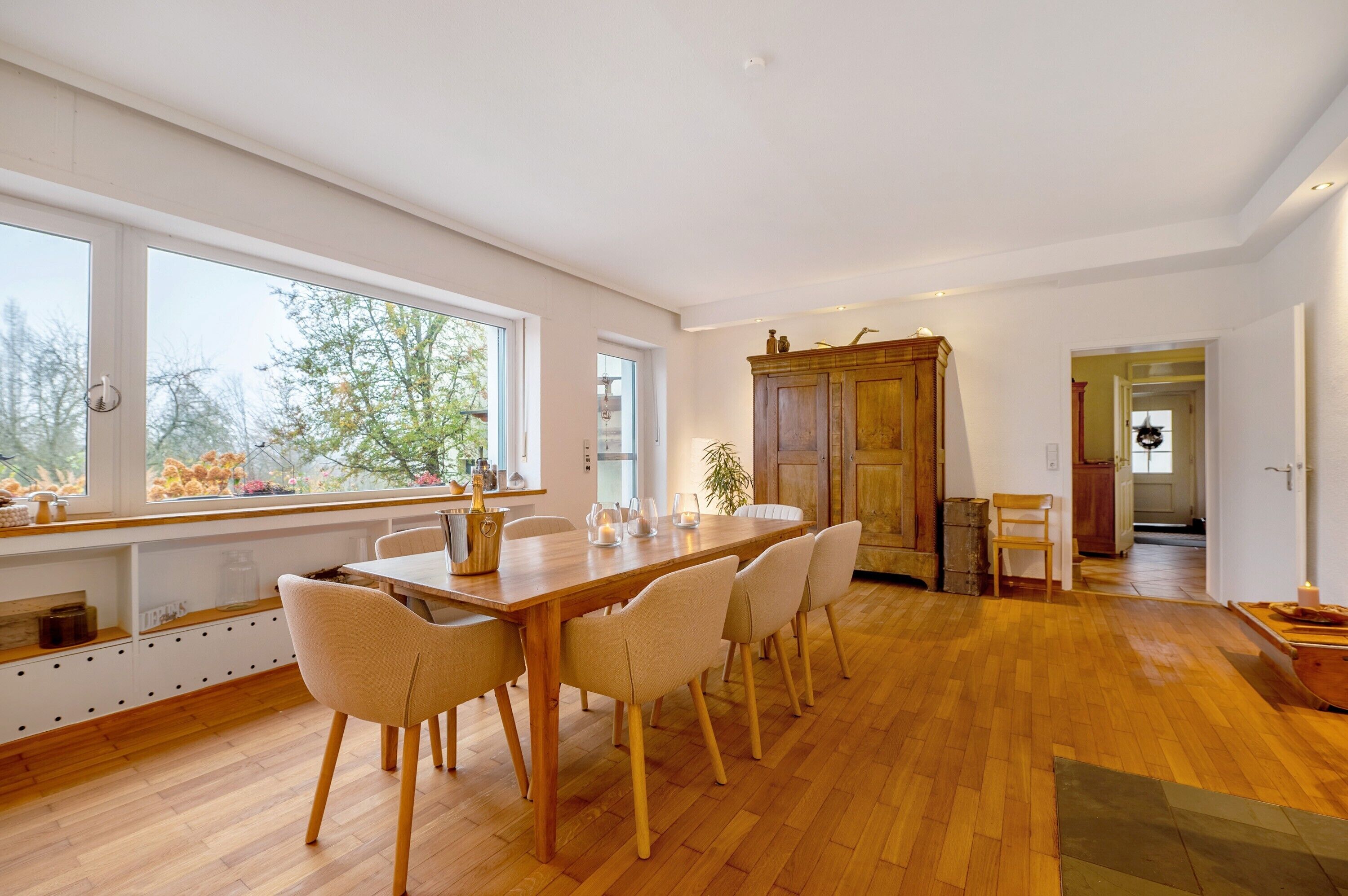 Un comedor amplio con una larga mesa de madera, seis sillas y vistas al exterior a través de grandes ventanales.
