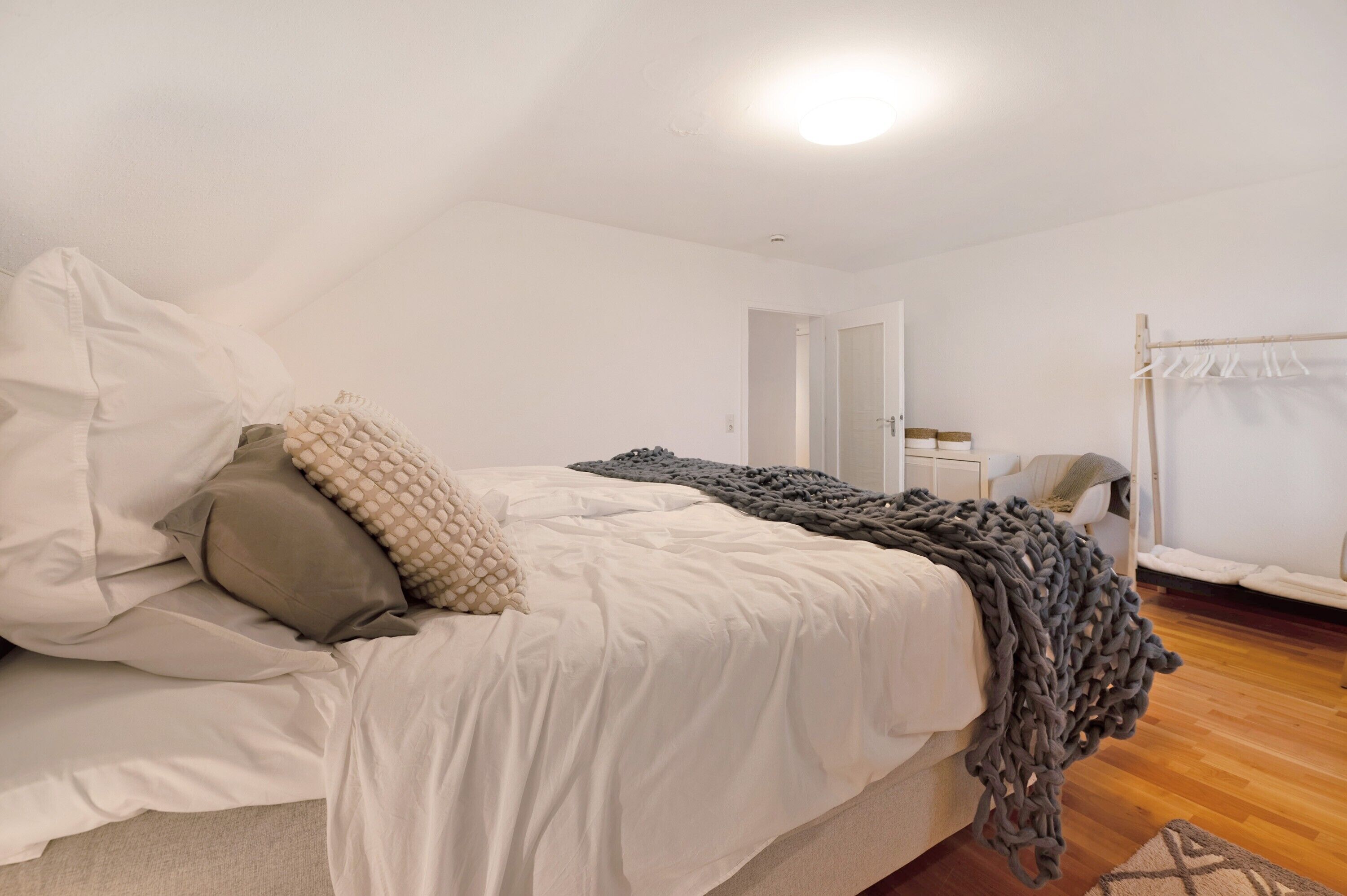 Een slaapkamer met een bed, kussens, een deken, een deur en een hangstoel.