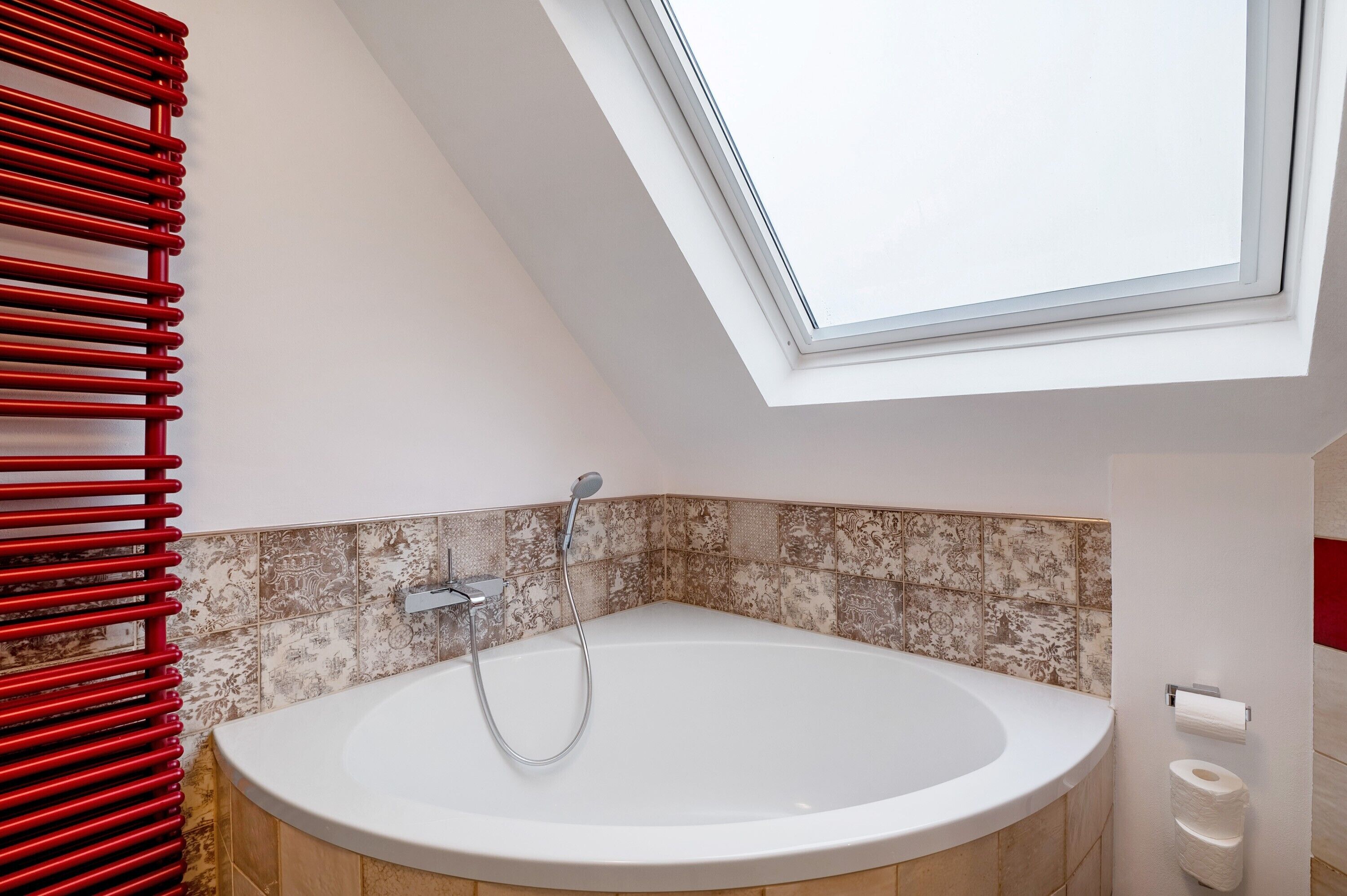 Een moderne badkamer met dakraam, badkuip, rode handdoekhouder en behangtegels.