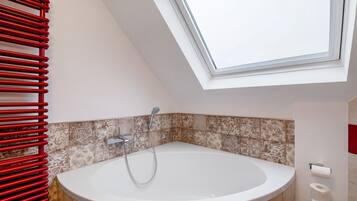 Een moderne badkamer met dakraam, badkuip, rode handdoekhouder en behangtegels.