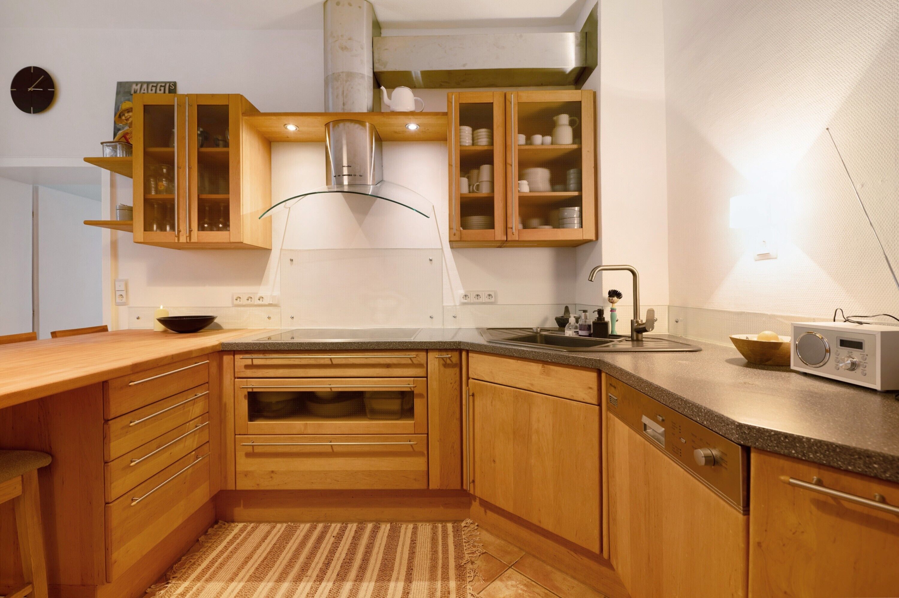 A kitchen with wooden cabinets, a stainless steel range hood, a built-in oven, a sink, and a radio.