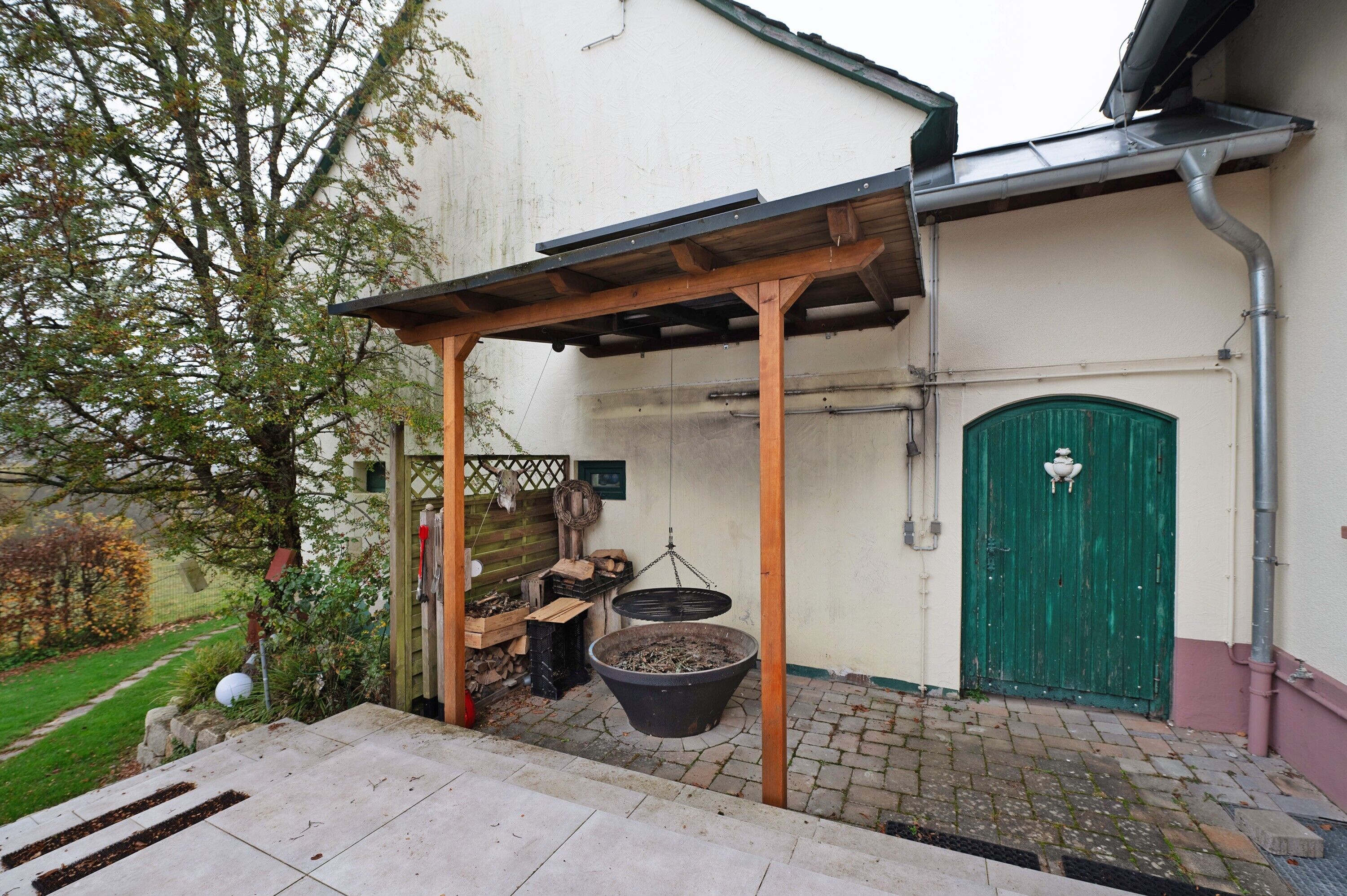 A covered outdoor area with a wooden pergola, a green door, and a large black pot.