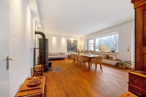 Eine moderne Küche mit Einbauherd, Holzboden, einer Essecke mit Tisch und Stühlen sowie einem großen Fenster mit Blick ins Freie.