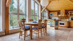 Een houten interieur met een eettafel en stoelen, grote ramen en een keukenhoek.