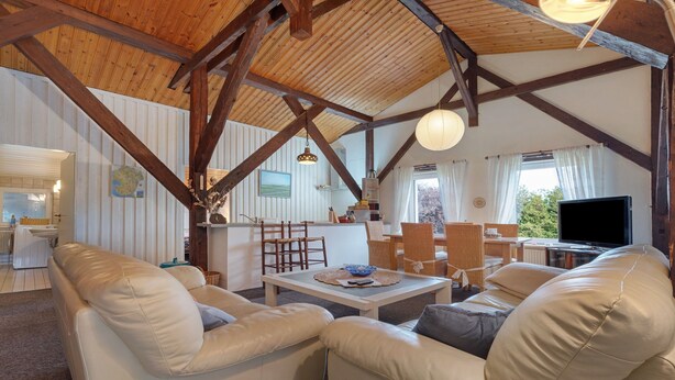 Amplia sala de estar con techo de madera alto, televisor y comedor con sillas y mesa.