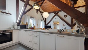 Una cocina con armarios blancos, horno empotrado, un lavabo y techo de madera.