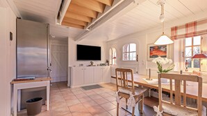 Une cuisine spacieuse avec des meubles blancs, une table à manger en bois et un téléviseur fixé au-dessus du comptoir.