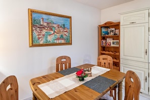 Un comedor con una mesa de madera, sillas, un cuadro, una estantería y un armario blanco.