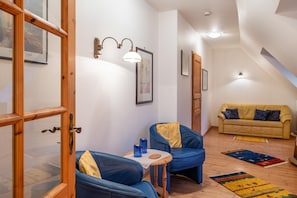Una habitación acogedora con una puerta de madera, dos sillones azules, una mesita, un sofá amarillo y una lámpara en el techo.