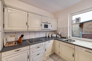 Una cocina con armarios blancos, encimera negra, microondas, lavabo y ventana con vistas a un edificio de ladrillo.