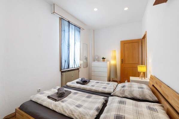 A bedroom with two beds, a dresser, a mirror, a lamp, and a window with curtains.