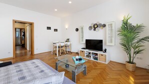 Una sala de estar moderna con una mesa de centro de vidrio, un sofá, un televisor, un comedor y una planta en maceta.