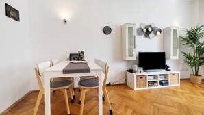 Una sala de estar moderna con una mesa de comedor, sillas, un televisor de pantalla plana, un mueble con objetos decorativos y una planta en maceta.