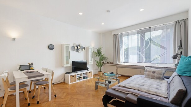 Una sala de estar moderna con un sofá, un televisor, una mesa de comedor con sillas, una estantería y un ventanal con cortinas.