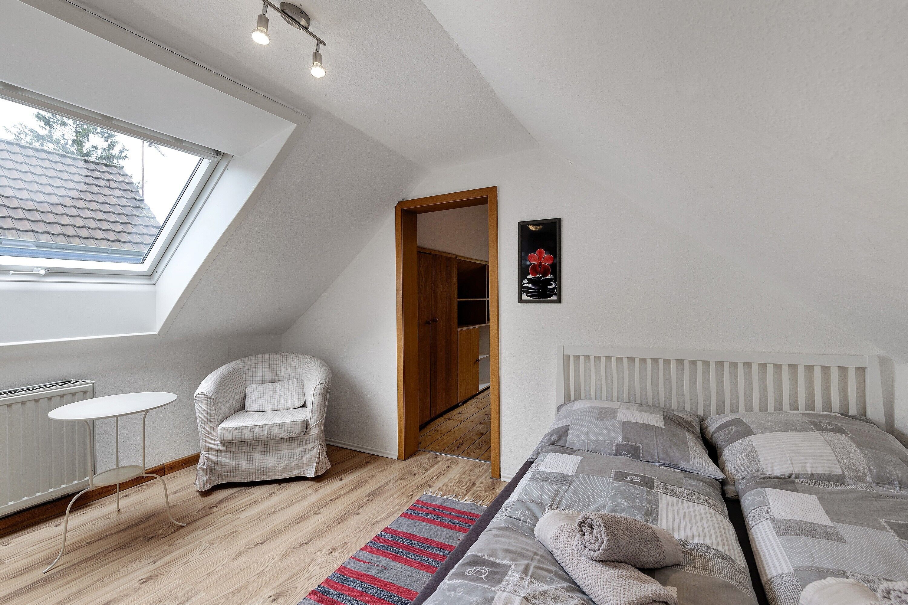A bedroom with a skylight, a bed, a chair, a small table, and a radiator.