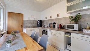 A modern kitchen with a wooden dining table, grey chairs, and white cabinets.