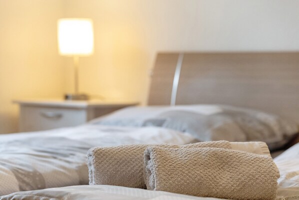 A neatly made bed with a headboard, a bedside lamp, and a nightstand.