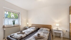 A bedroom with two beds, a window with a view, bedside tables with lamps, and a radiator.