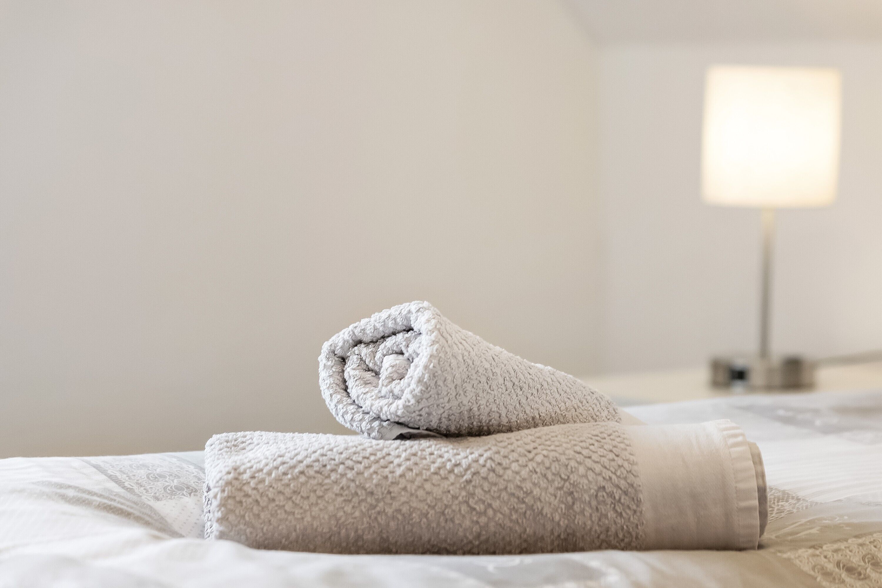 Cama bem arrumada com uma toalha enrolada e um abajur.