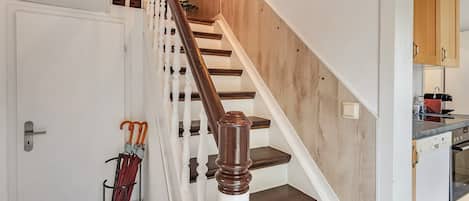 Un escalier avec des marches en bois et des balustrades blanches, une porte avec une poignée, et un porte-parapluie fixé au mur, contenant des parapluies.