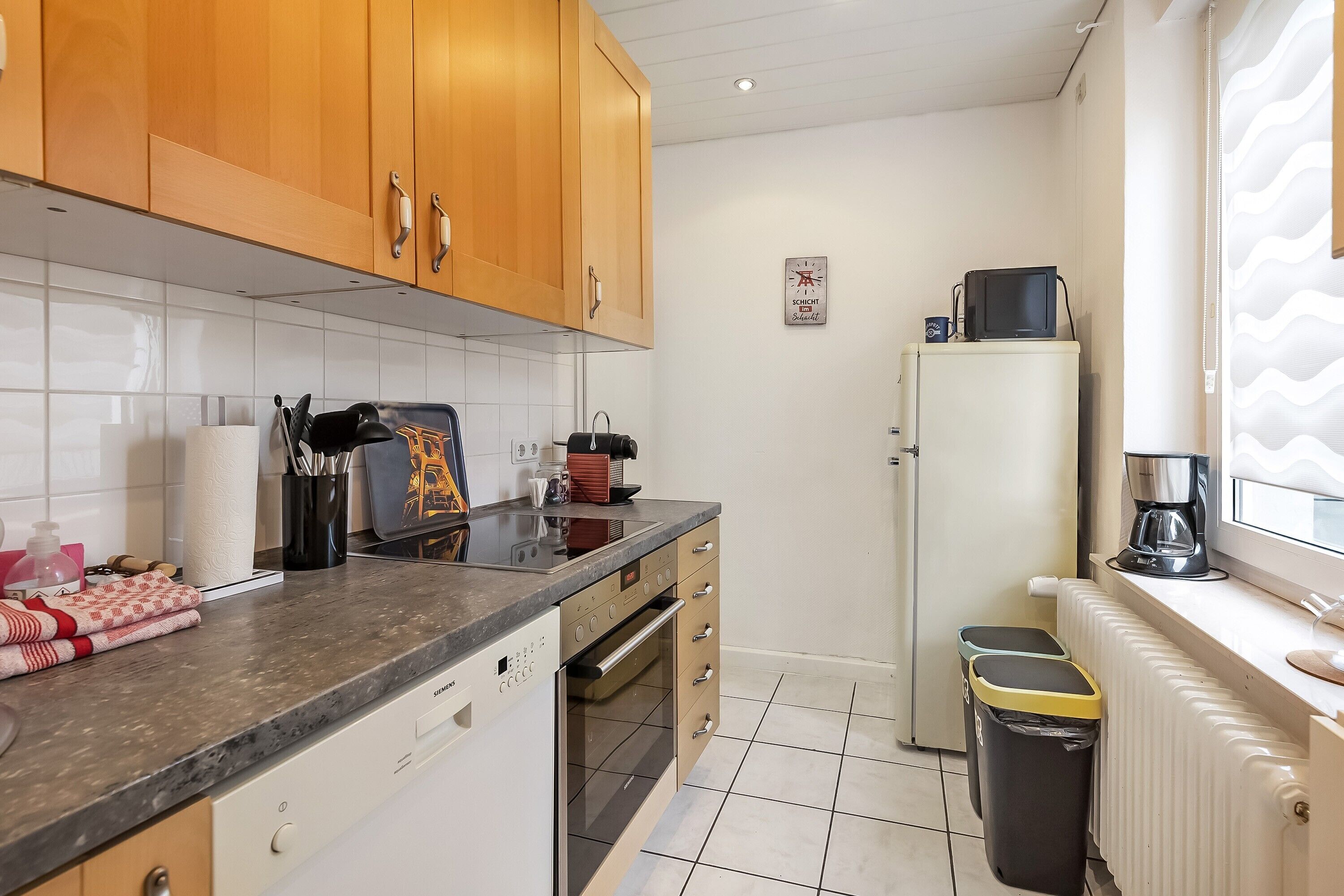 Cocina compacta con armarios de madera, horno empotrado, refrigerador y cafetera sobre la encimera.