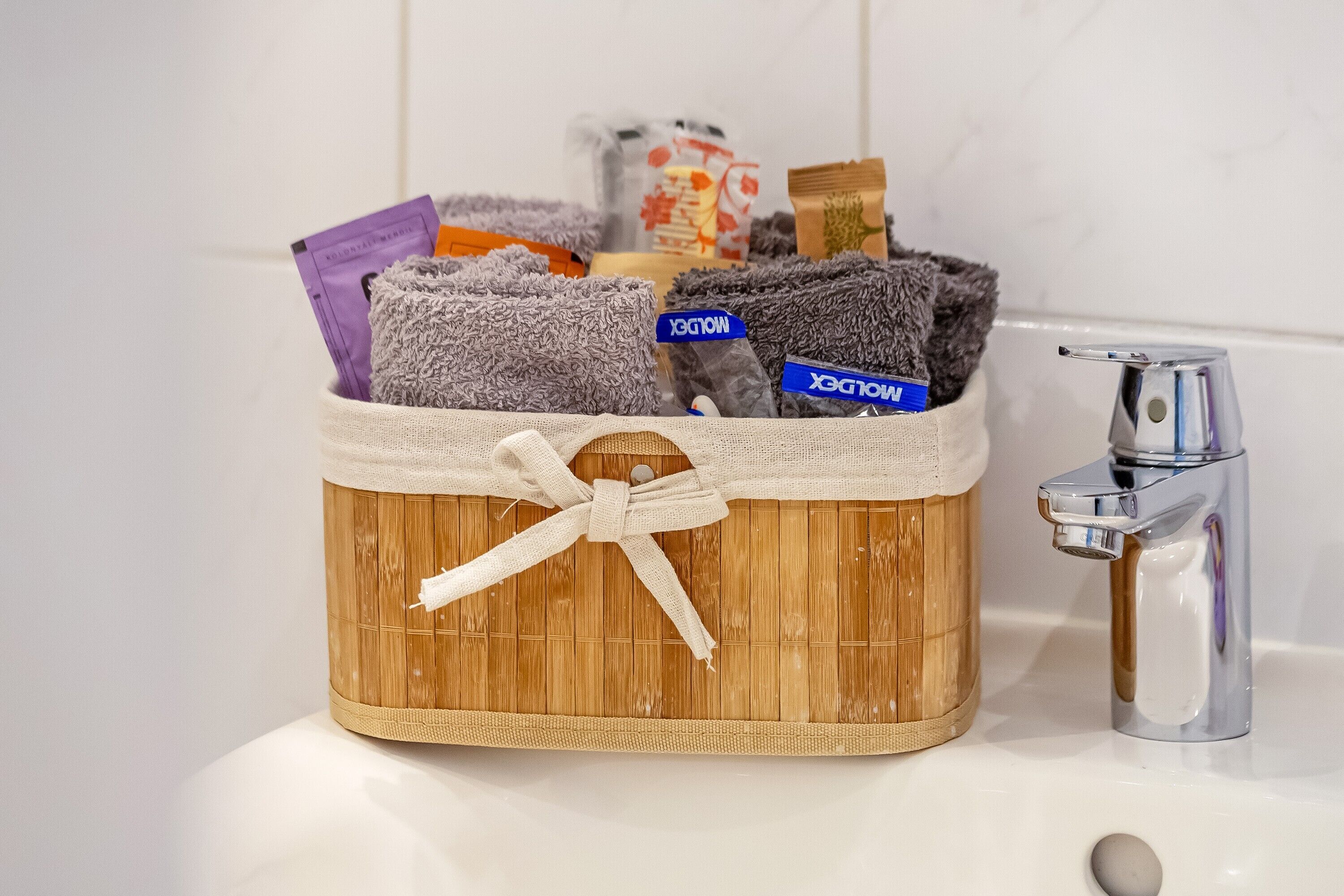 Un panier en bois muni d’un cordon de serrage, contenant divers articles, notamment une serviette violette, une serviette grise et une étiquette bleue portant l’inscription « MOLDEX ».