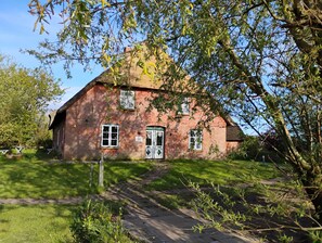 A brick house with a thatched roof, a front door, and a small garden area.