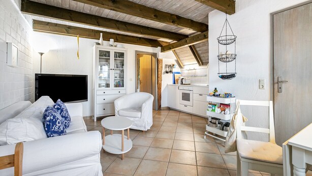 A modern kitchen with white cabinets, a dining area with a white table and chairs, and a living area with a sofa and a TV. - Apartment 1 with Shared Garden, Terrace, and Wi-Fi (Rodenäs)