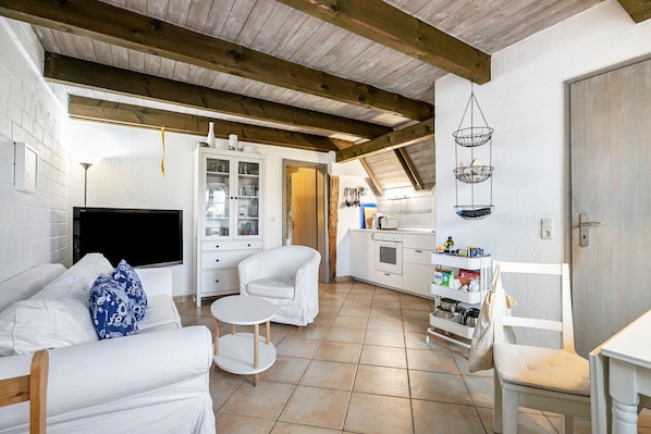 A modern kitchen with white cabinets, a dining area with a white table and chairs, and a living area with a sofa and a TV.