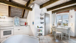 A kitchen with wooden beams, a white stove, a window, and a dining area with a table and chairs. - Apartment 1 with Shared Garden, Terrace, and Wi-Fi (Rodenäs)