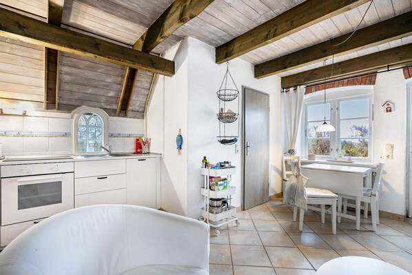 A kitchen with wooden beams, a white stove, a window, and a dining area with a table and chairs. - Apartment 1 with Shared Garden, Terrace, and Wi-Fi (Rodenäs)
